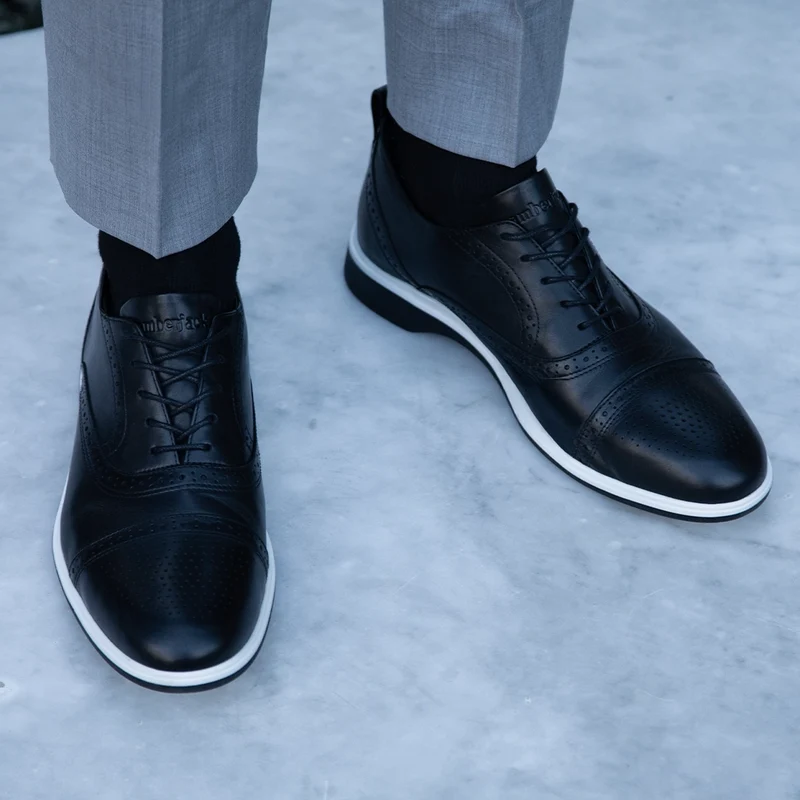 The Cap-Toe in Onyx Black and White worn by model with light gray dress pants
