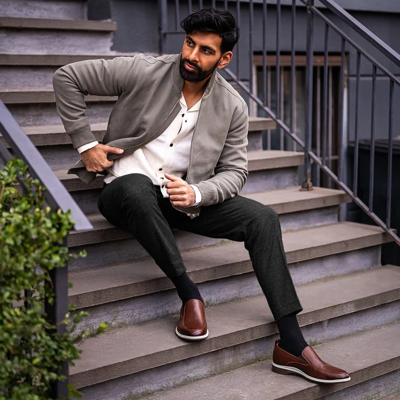 Model sitting on steps wearing The Slip-On Coffee paired with dark dress pants and green jacket