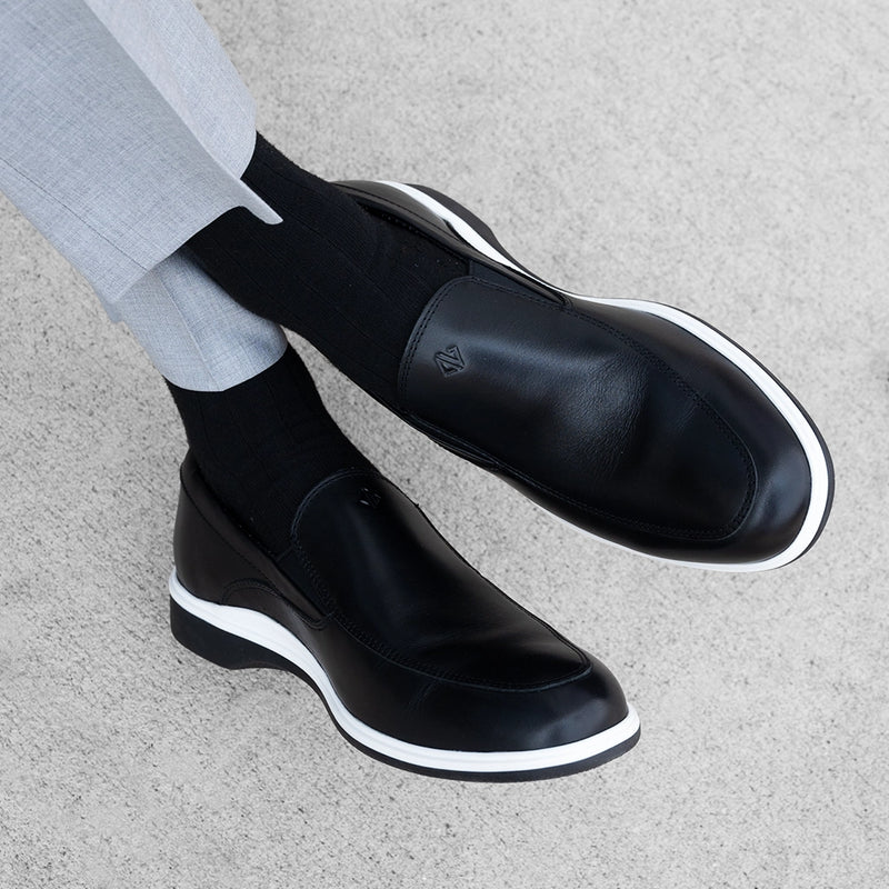 Close-Up of model wearing The Slip-On in Onyx paired with black dress socks and light gray pants